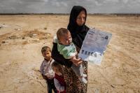 Syrian refugee mother with her two children in the desert like area in Jordan and their UNHCR registration paper. 