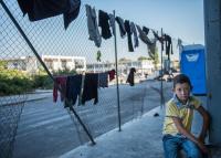 Afghani refugee boy watching the families drying clothes on the fence in the old airport in Athens, Greece. 